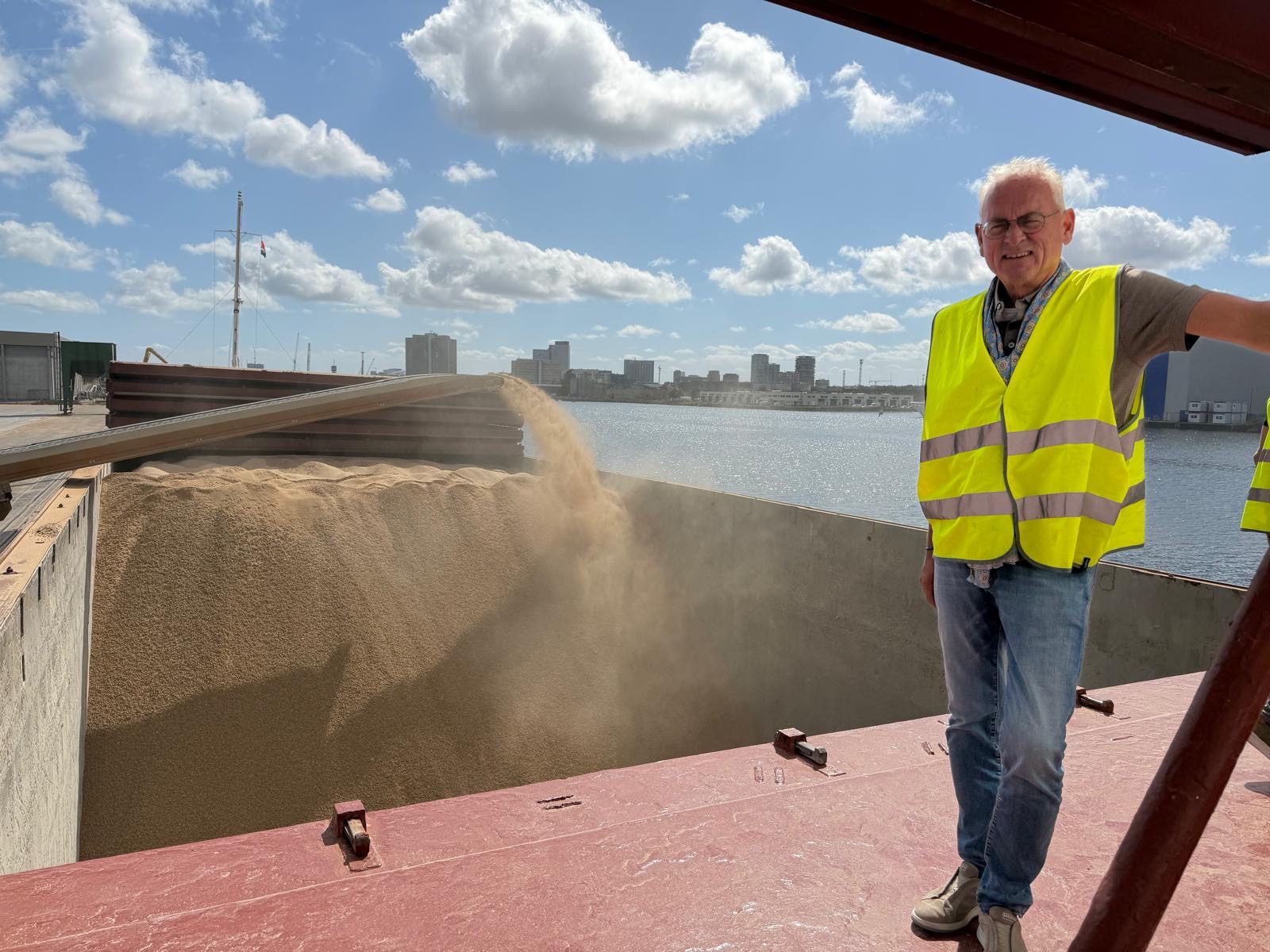 Pieter-Paul Verhorst in hesje aan boord van een schip, terwijl er graan in het ruim wordt gestort
